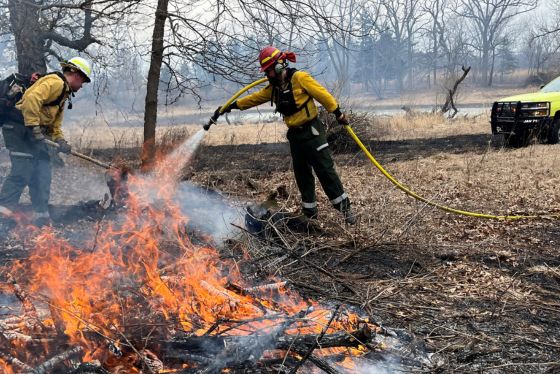 firefighters weilding hoses work to put out an escaped fire that originated in a burn pile