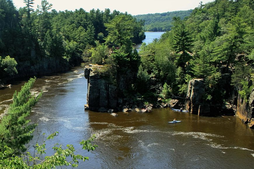 Scenic view of the St. Croix River with lush greenery and a kayak on the water, surrounded by rocky cliffs.