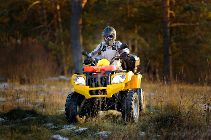 portrait of a man in helmet and safety goggles looking into the camera while sitting on all-terrain vehicle against snowy late autumn landscape