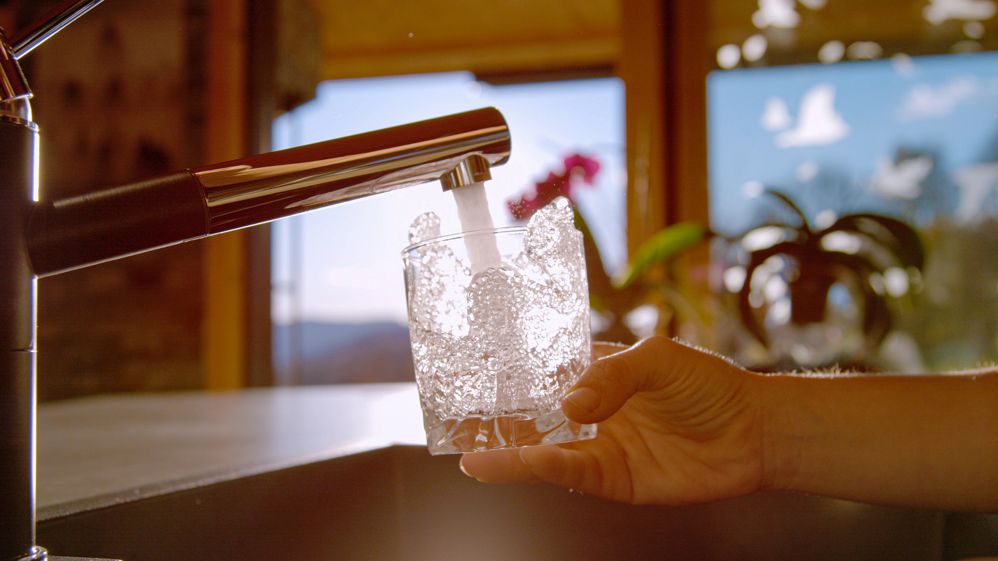 a hand filling up a glass of water from the faucet in a kitchen