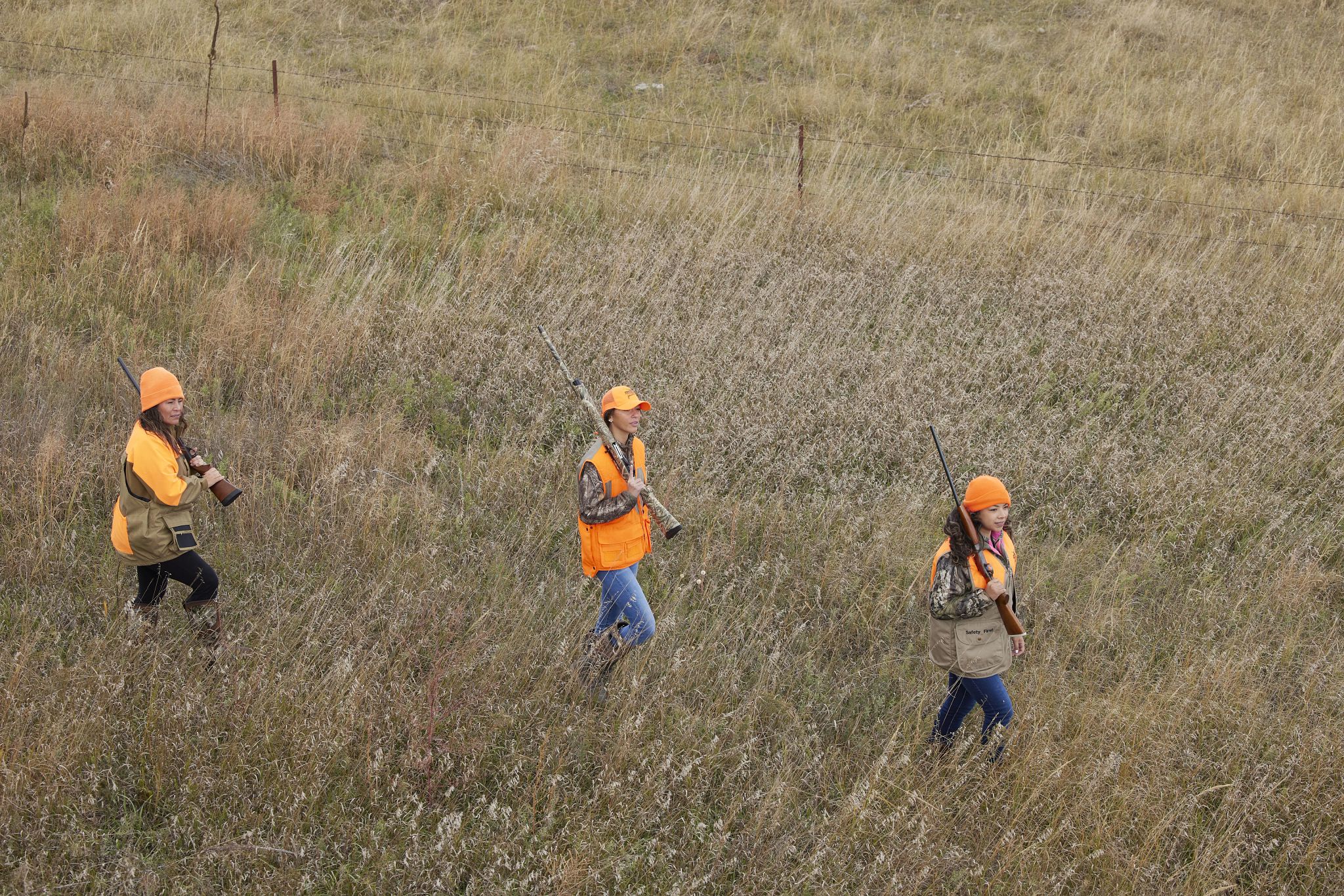 Three female hunters wearing blaze orange walking in a field