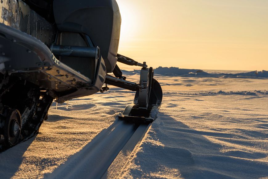 A snowmobile stands on the snow at sunset.