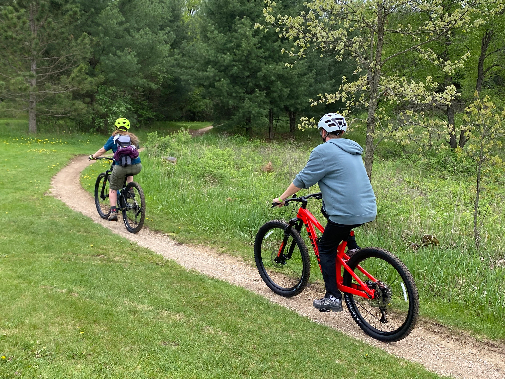 Two bicycle riders ride down a narrow bicycle trail in a lush green woods.