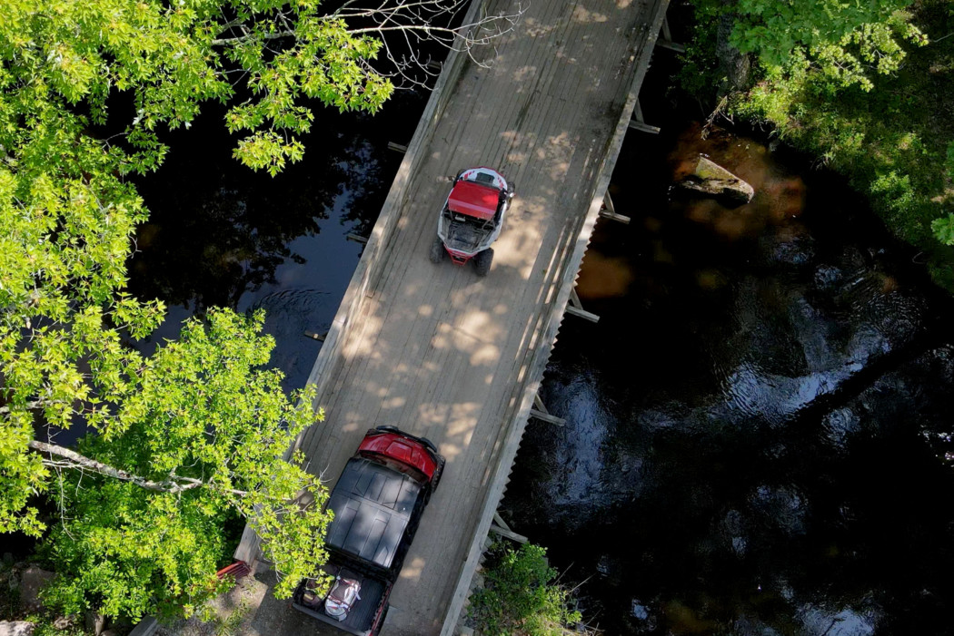 An aerial view of two red UTVs crossing a bidge, surrounded by lush green foliage.