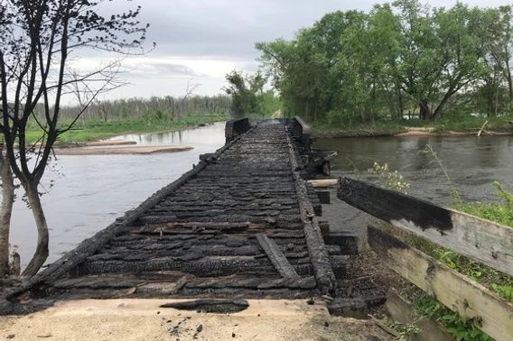 A charred wooden bridge over a river.