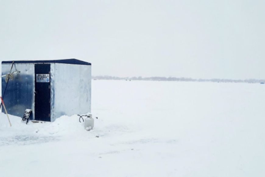 A metal ice shanty sits on a frozen lake covered in snow.