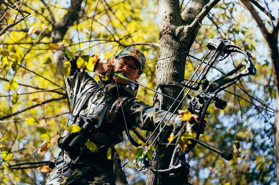 A young man hunting from a tree stand draws his bow.