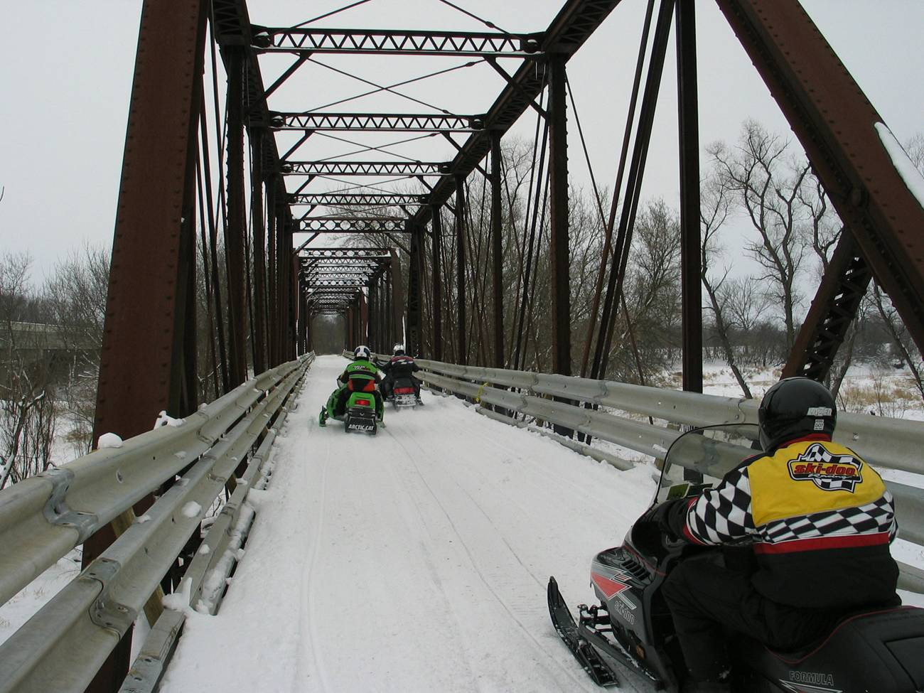 Snowmobilers ride on a pedestrian bridge in winter.