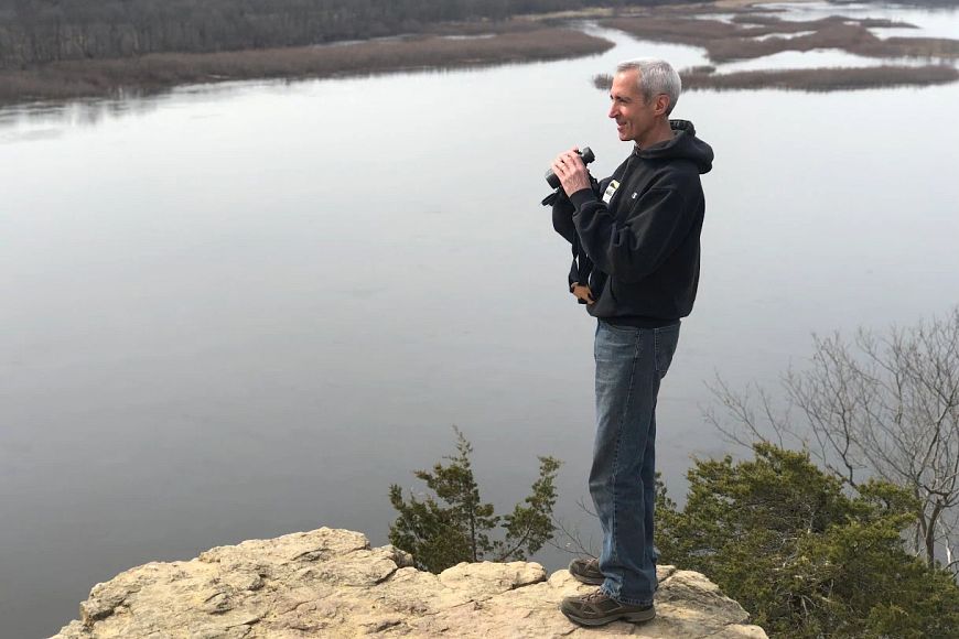 Thomas Meyer standing on a rock overlook, holding binoculars and looking into the distance.