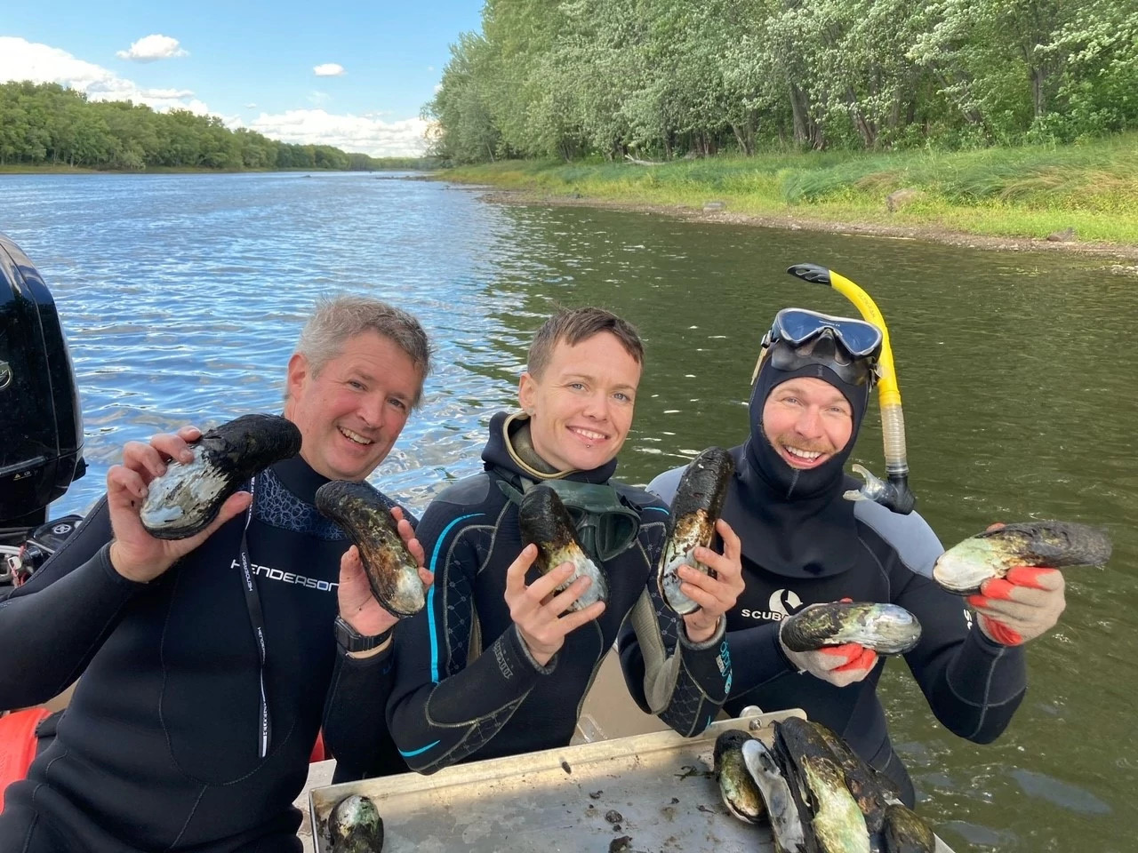 three people in st croix river holding mussels