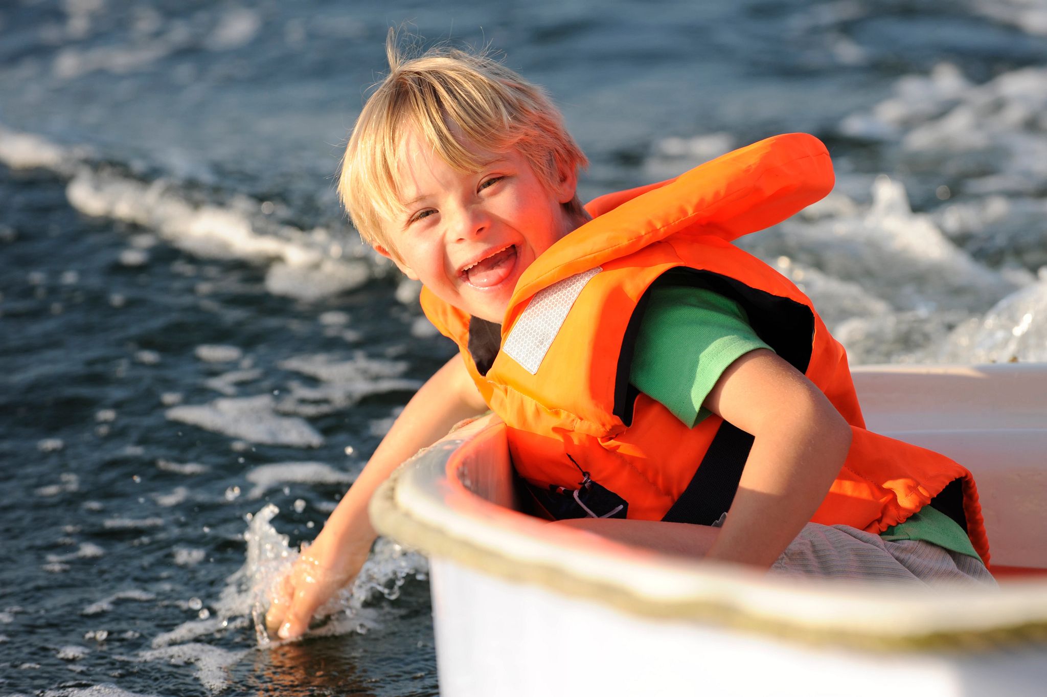 An image of a kid in a boat wearing an orange lifejacket. 