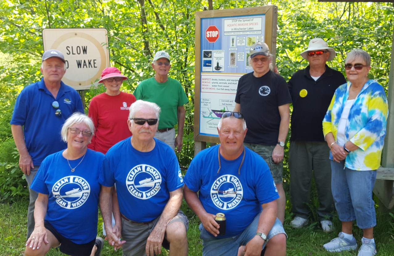 volunteers pose in front of invasive species prevention sign
