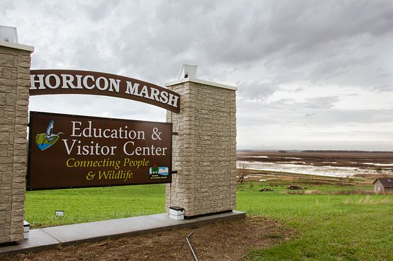 The Horicon Marsh Education & Visitor Center sign on a cloudy day, with the marsh in the background. 