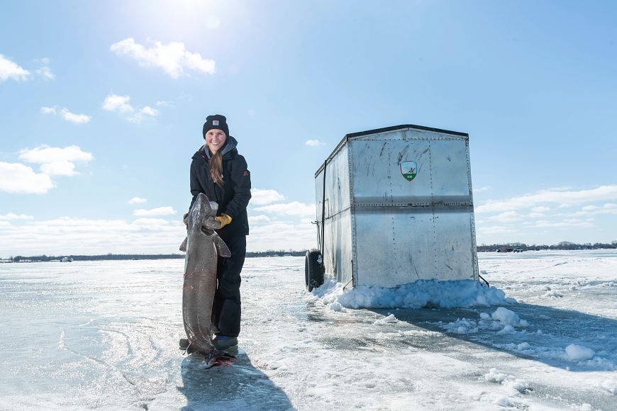 A woman holding up a sturgeon while ice fishing on the Upriver Lakes.