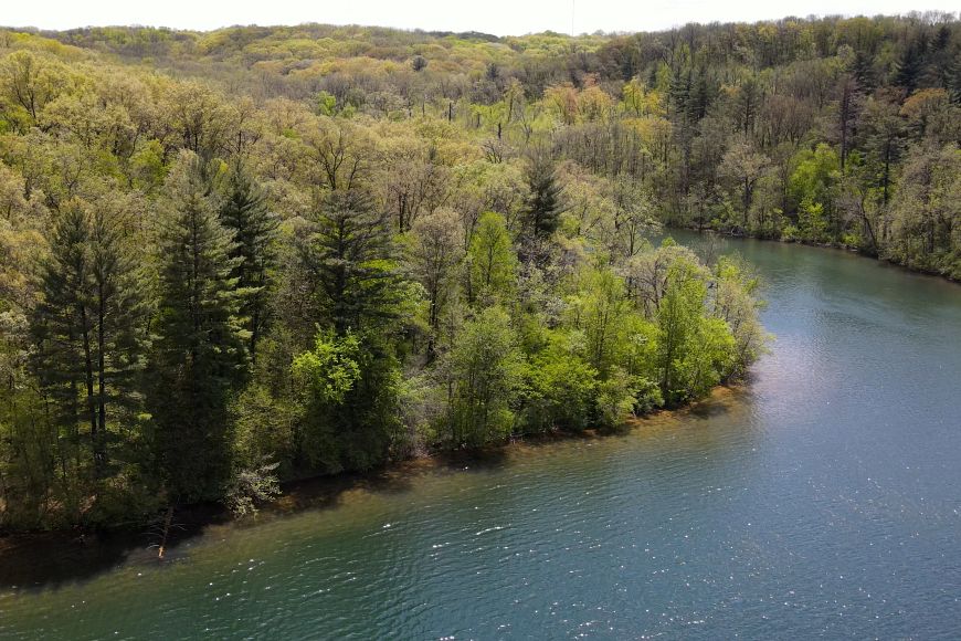 A drone view of a lake at Governor Dodge State Park in the springtime, with tall green trees along the banks.