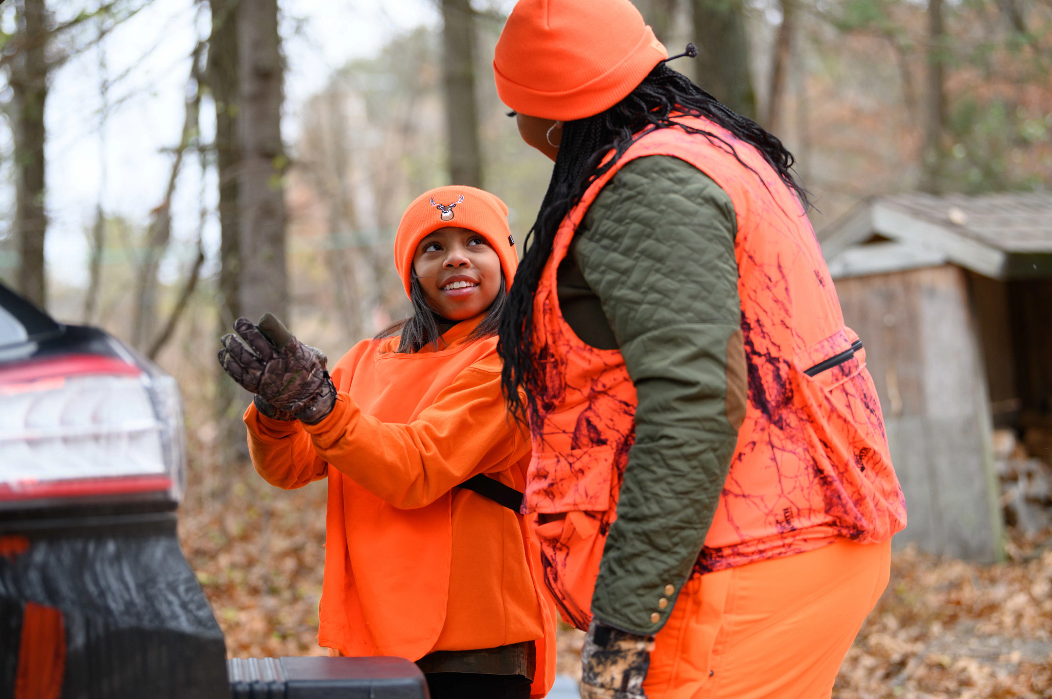 a young woman wearing blaze orange talks to another woman wearing blaze orange while preparing to hunt