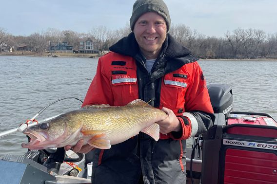 A man in an orange float coat holds a large walleye.