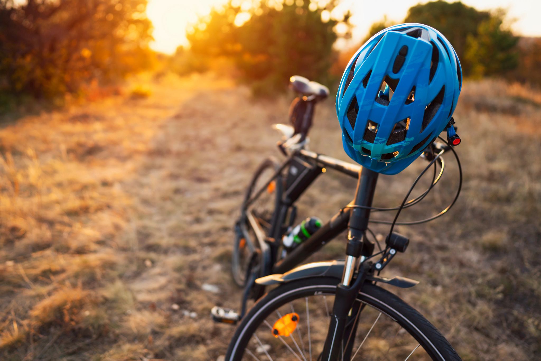 A closeup of a black bicycle and a blue helmet in a light brown nature area.