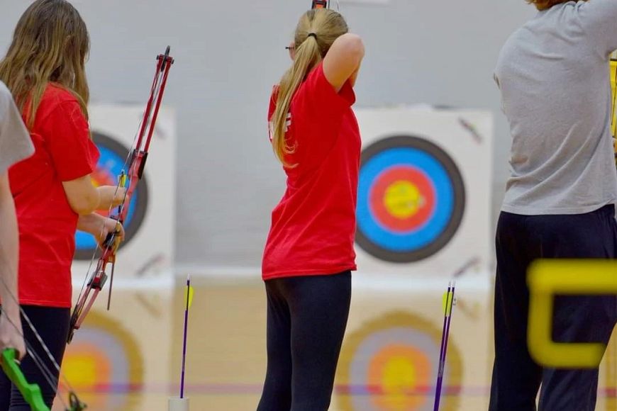 Three kids shooting a bow and arrows at an archery competition.