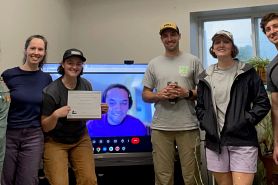 Five Green Box representatives pose with their award. A sixth representative joins on a computer screen via a video conference call in the center of the picture.