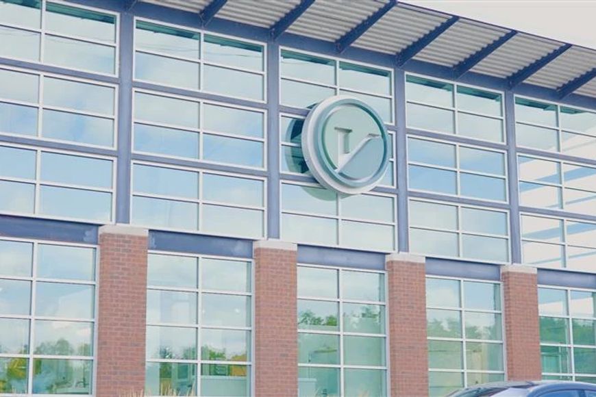 the outside of the Veridian Homes building with lots of windows, a green V logo and a car parked in front.