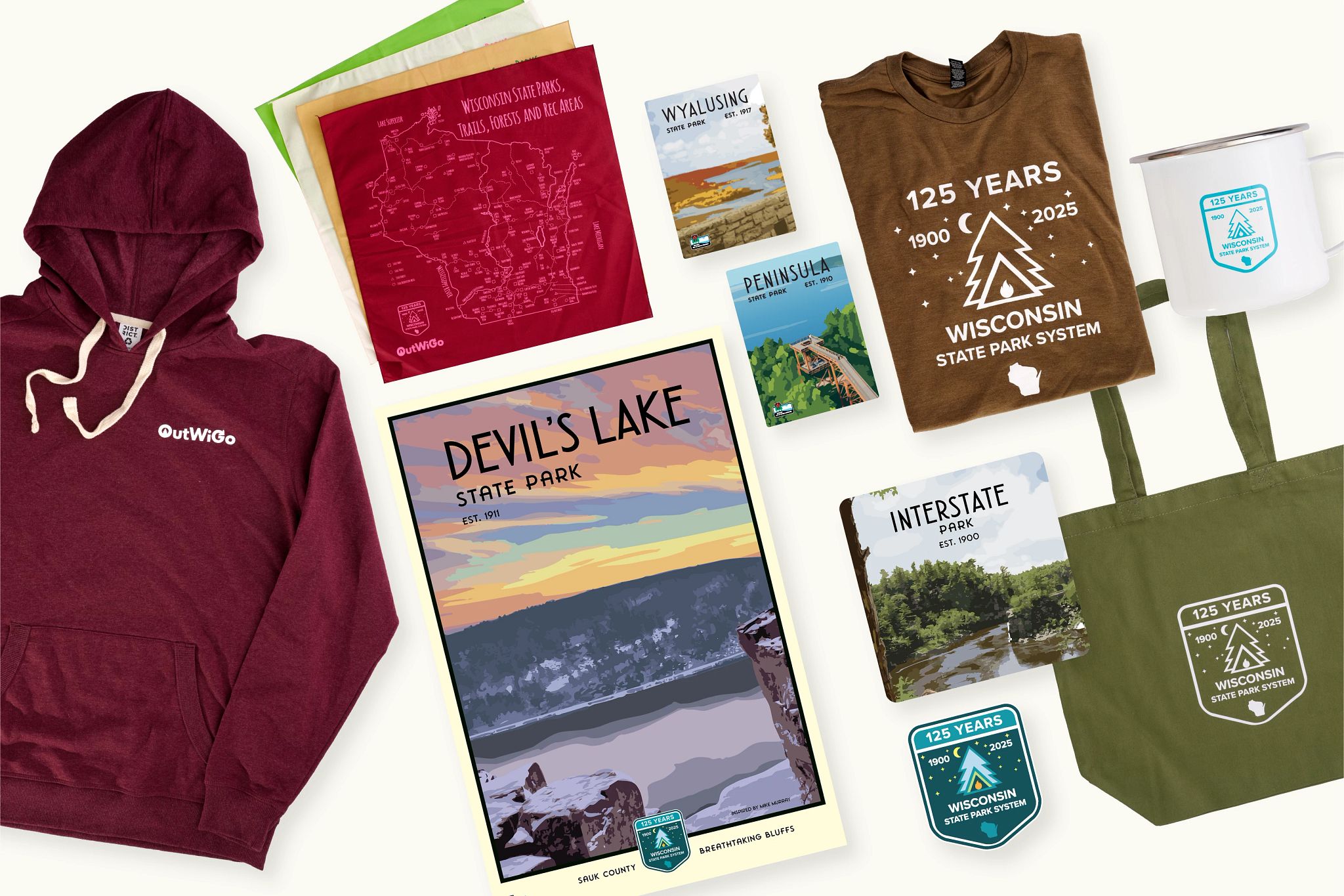 Assorted merchandise including a hoodie, t-shirts, cups, and posters promoting Devil's Lake State Park and Wisconsin State Park System, arranged on a plain background.