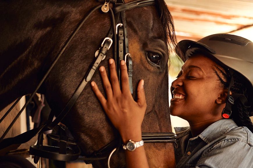 A young woman blissfully smiling big while holding her horse's face.