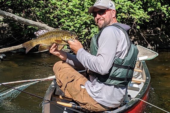 A man in a canoe and wearing a life jacket holds a beautiful smallmouth bass.