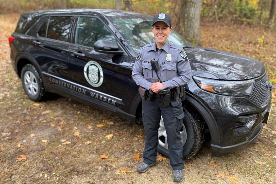 A DNR warden in front of a warden vehicle