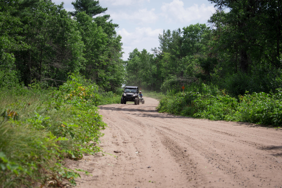 An ATV and a UTV ride toward the camera on a trail. 