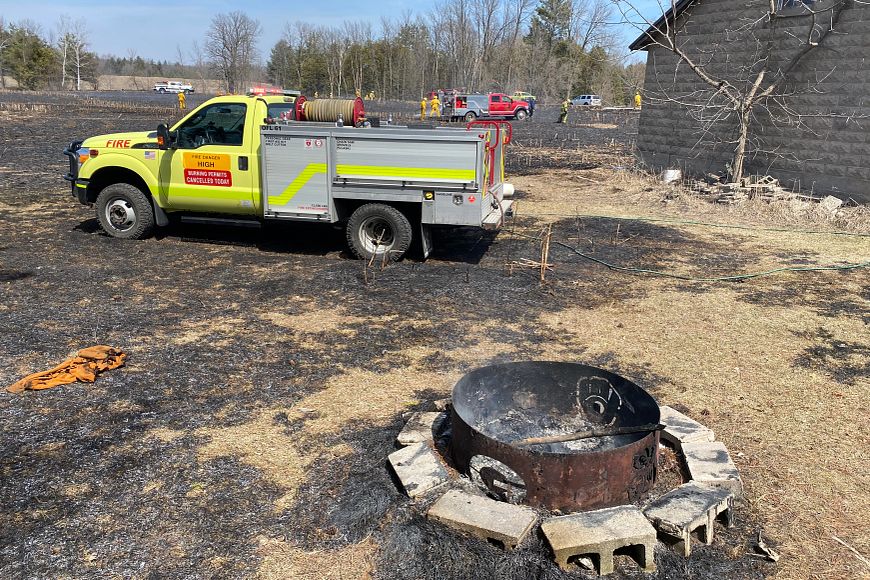 A DNR fire truck is parked next to a charred field with a fire pit in the foreground and other emergency vehicles in the background.