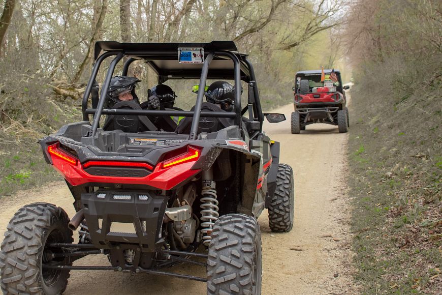 A group of people riding on two ATVs on a trail in a forest