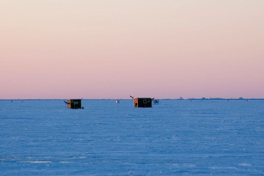 An two ice shanties sit on a frozen and snow covered lake.
