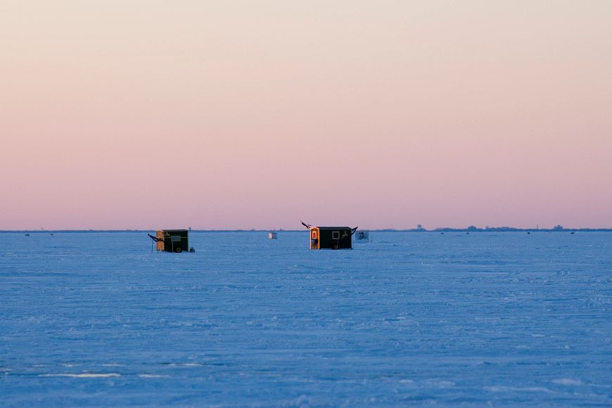 An two ice shanties sit on a frozen and snow covered lake. 