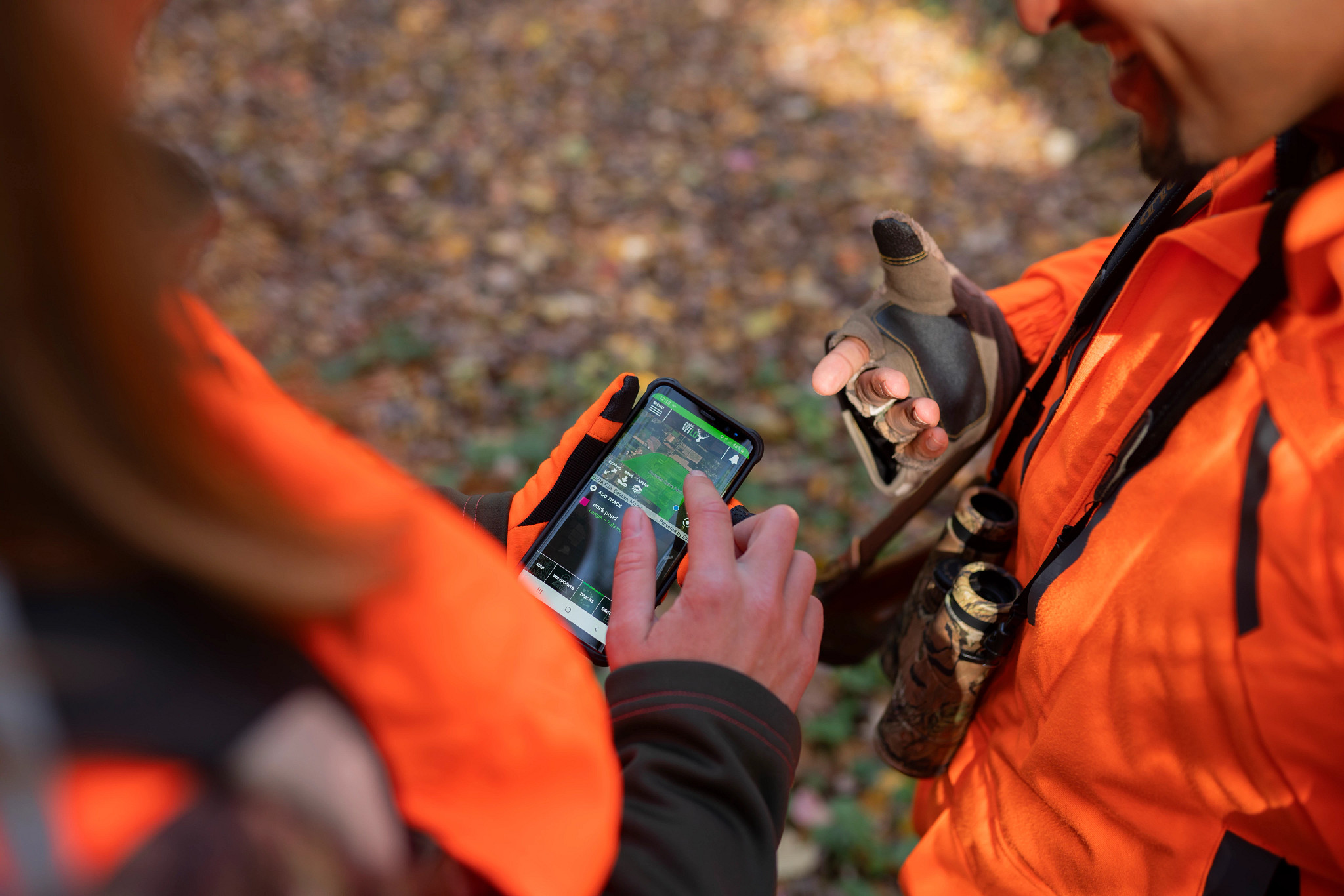 couple wearing blaze orange viewing Hunt Wild app on smartphone