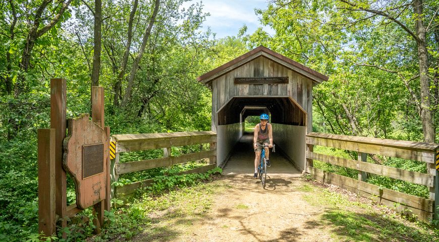 Bicyclist riding through a covered bridge on the Sugar River State Trail