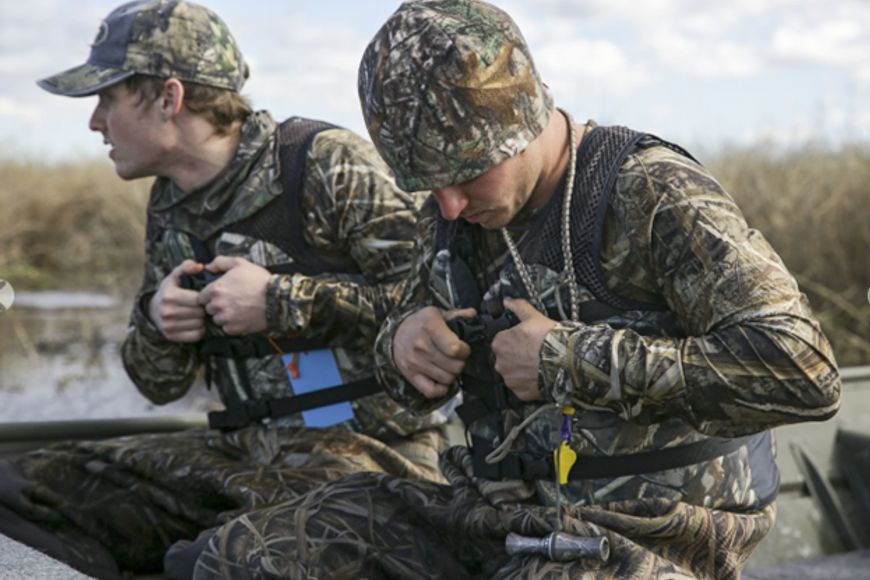 two hunters in camouflage on a boat in wetlands