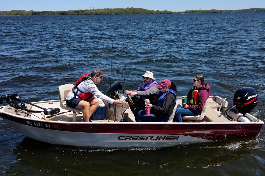 four people wearing life jackets on a boat on a lake with snacks and water bottles