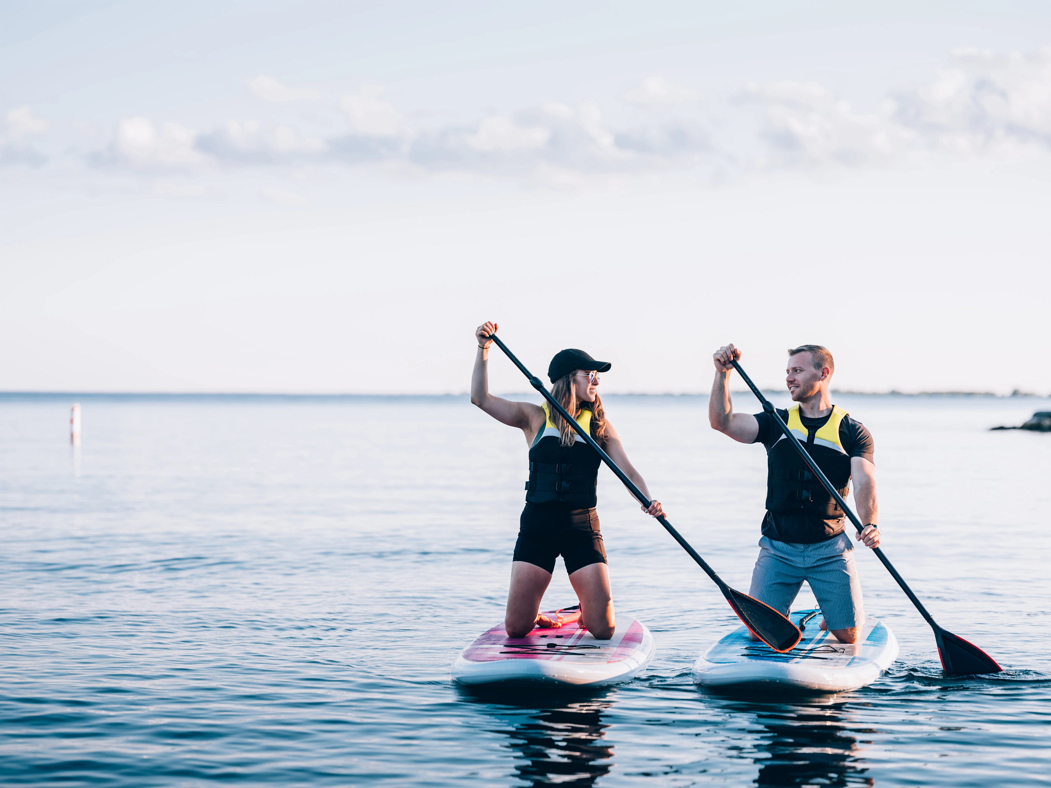 a man and woman wear life jackets while paddleboarding