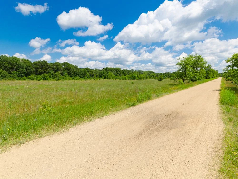sunny day on a gravel trail with a prairie to the left.