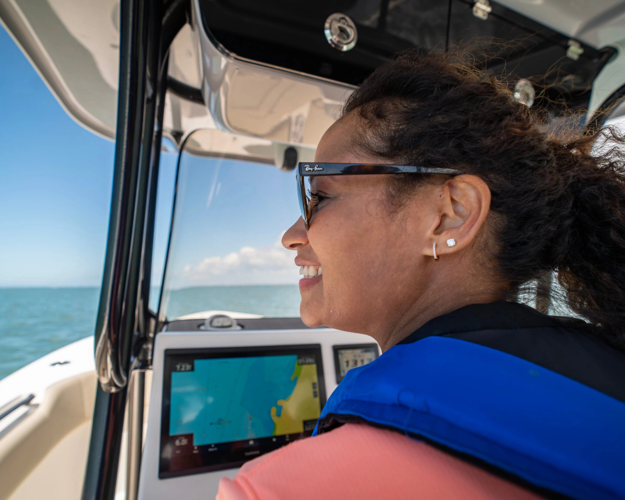 A woman driving a boat wearing a life jacket. 