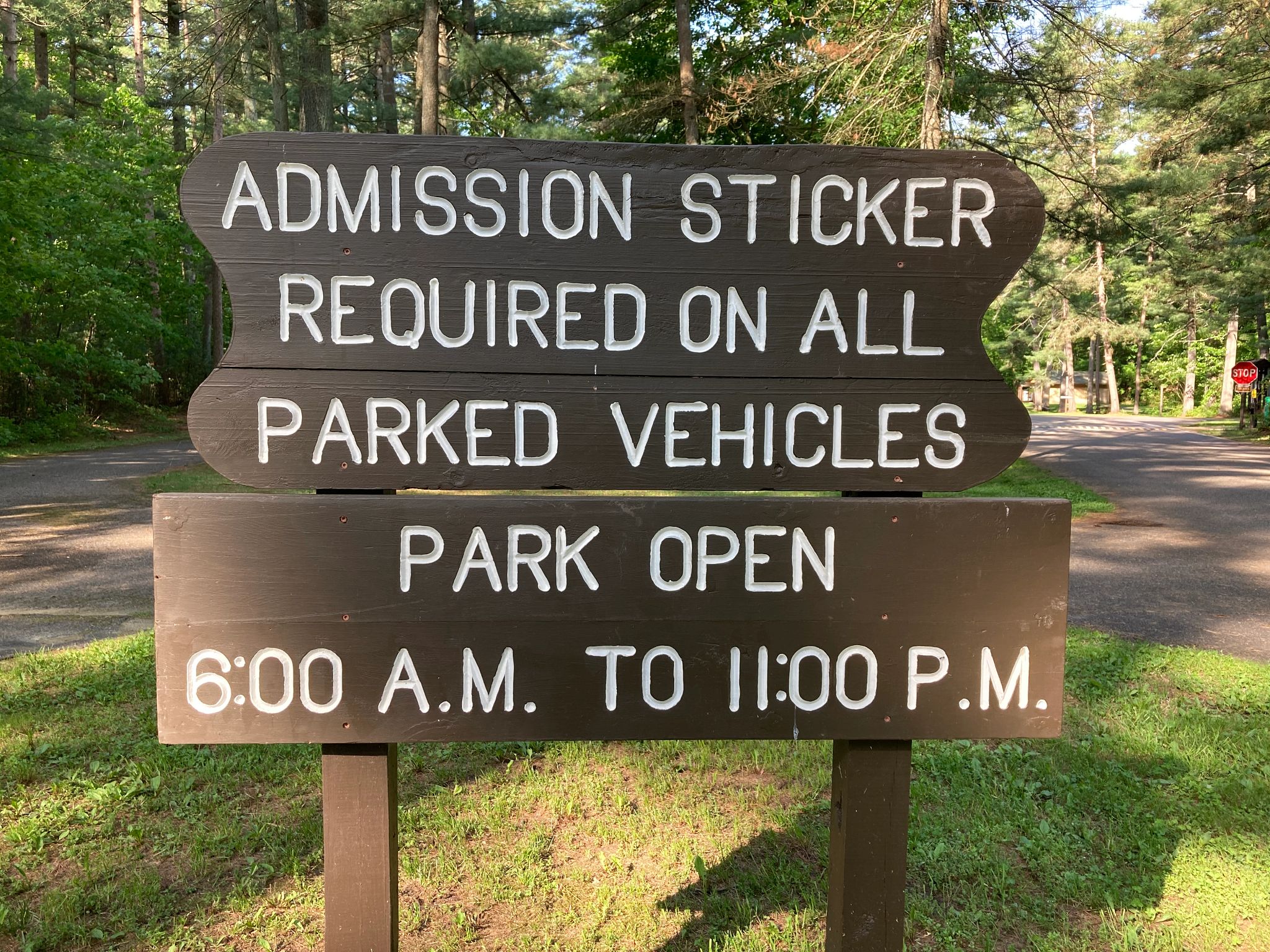a brown sign for vehicle admission stickers in a green forest