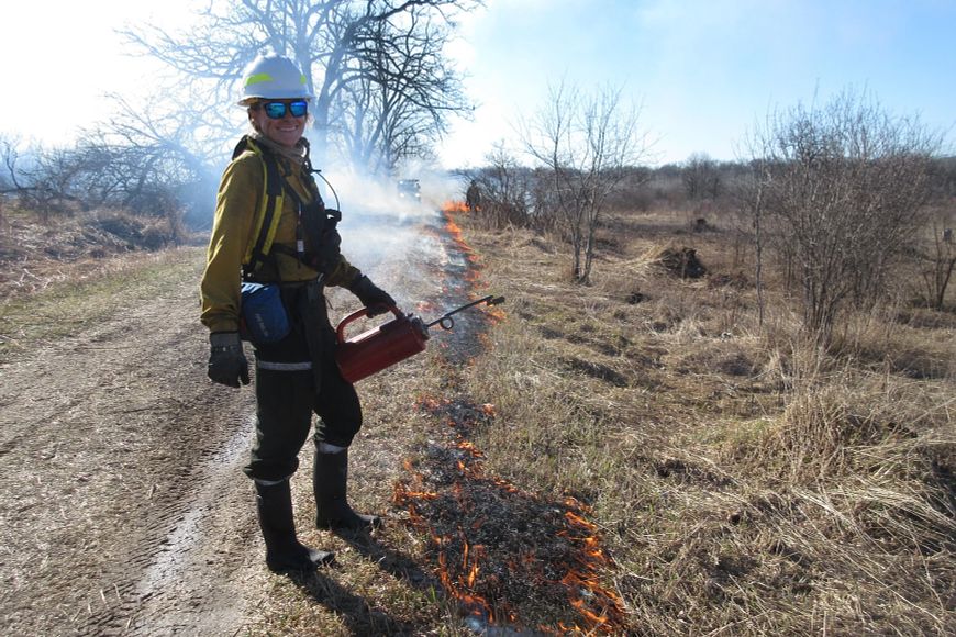 A male with safety gear doing a prescribed burn in a grassy area
