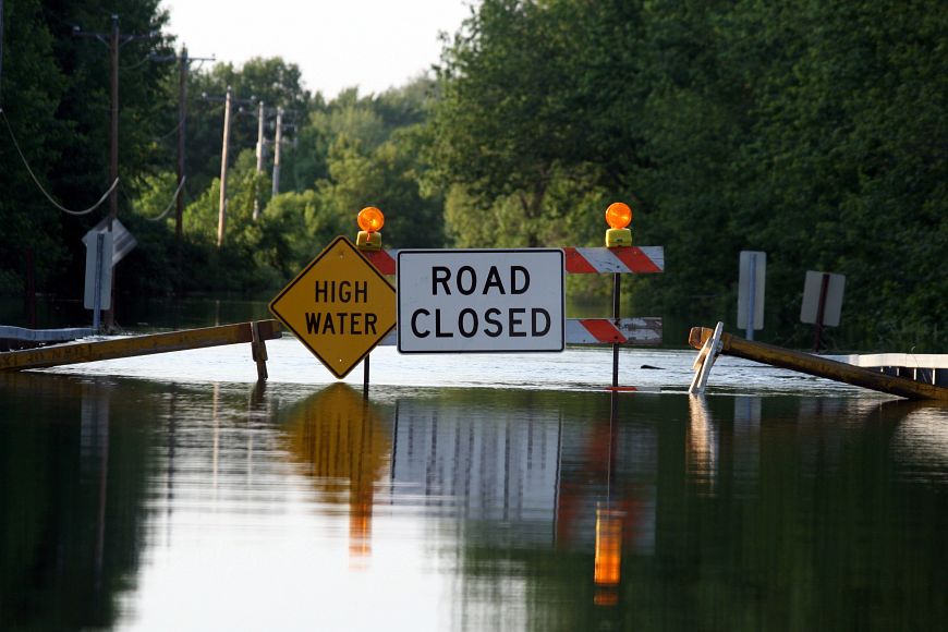 Two signs, reading "high water" and "road closed" block a road that is flooded. 