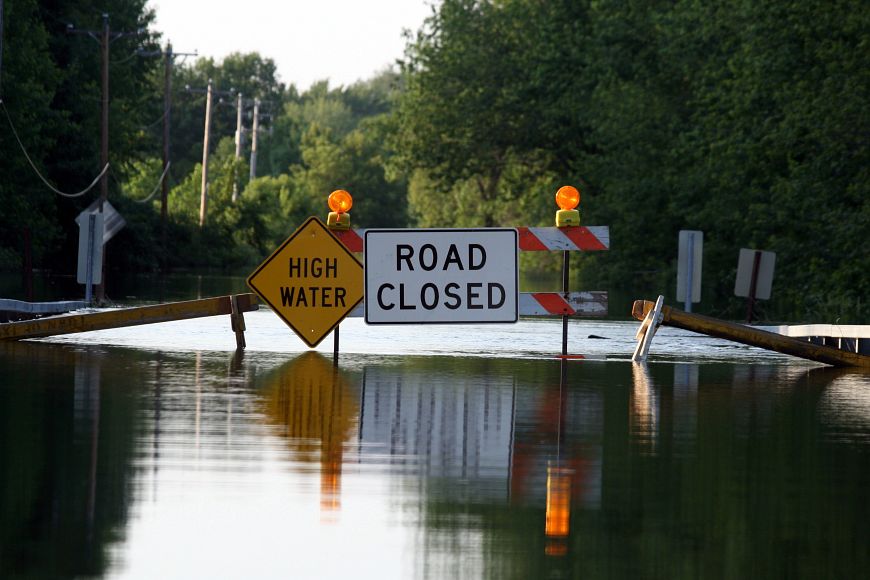 Two signs, reading "high water" and "road closed" block a road that is flooded.