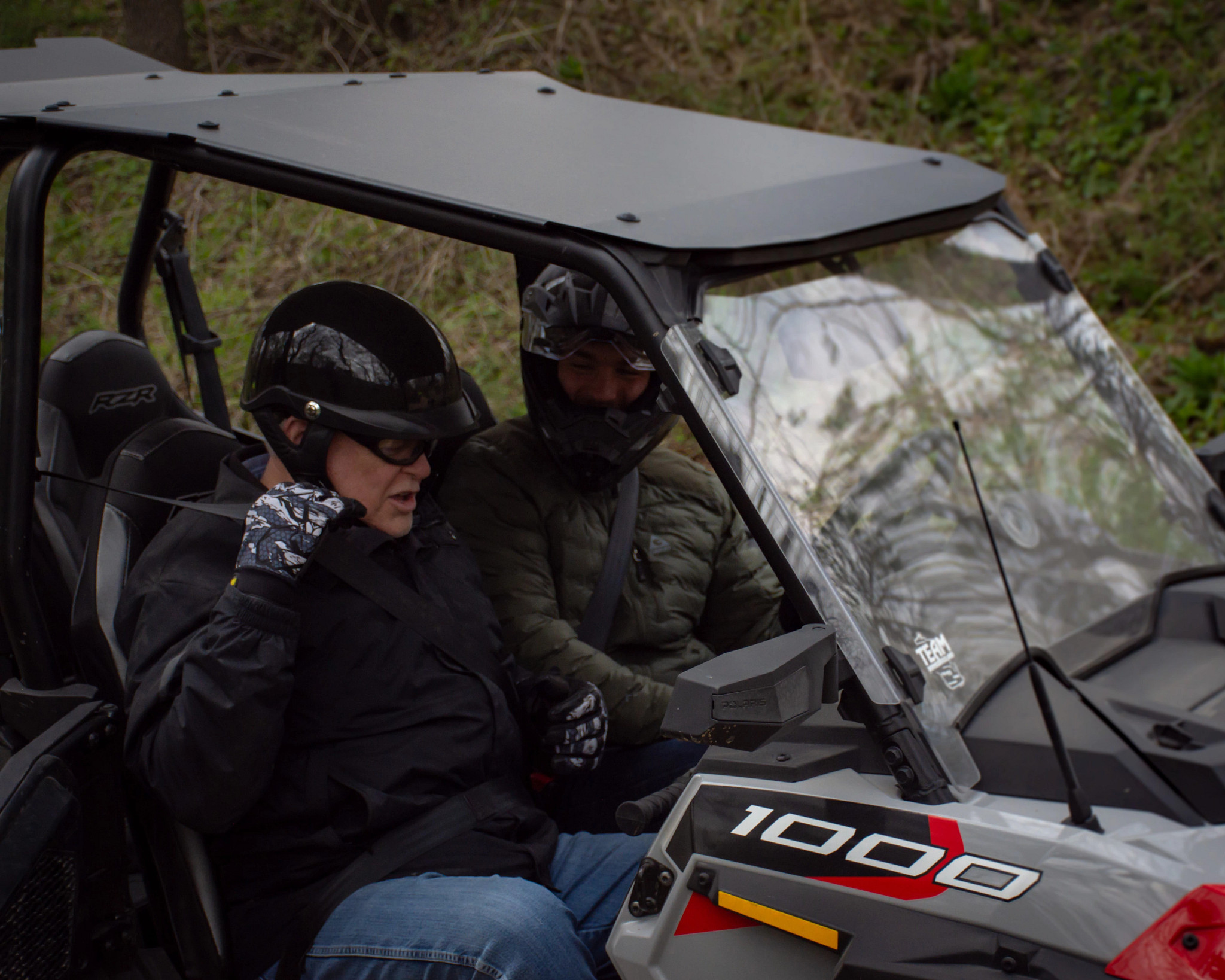 Two people ride in an ATV, helmets fastened. 