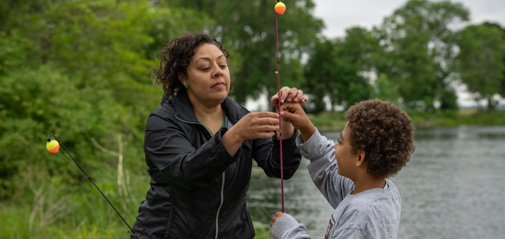 A woman is teaching a child to fish and how to set up a fishing pole.