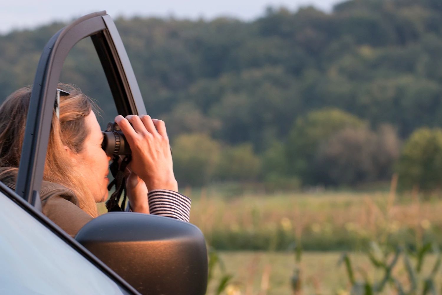 An image of a woman looking through binoculars while sitting in a vehicle.