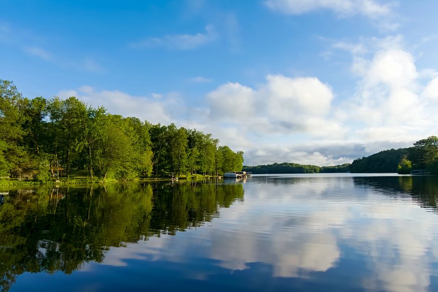 a calm Wisconsin lake surrounded by trees under a blue, cloudy sky