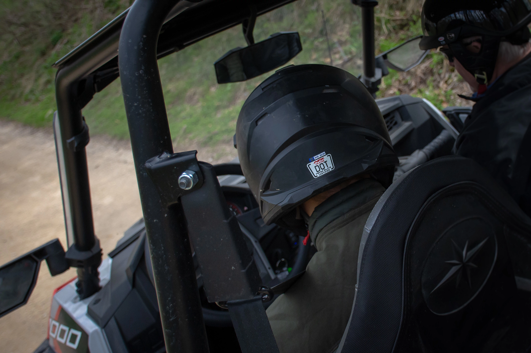 The back of two helmeted passengers' heads in a UTV. 